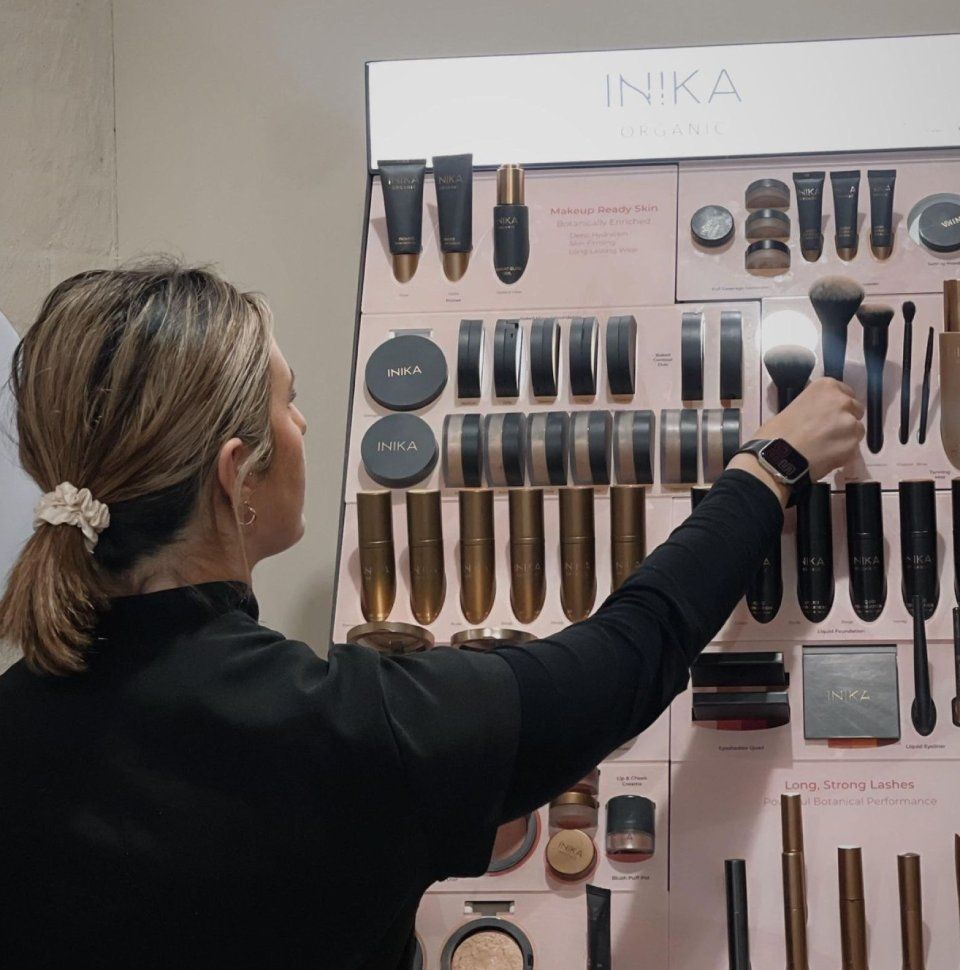 Woman reaching for makeup brush on display of INIKA cosmetics.