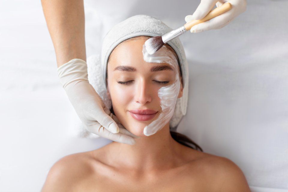 Person receiving facial treatment, white cream mask applied by a gloved hand.