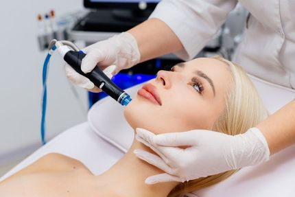 Woman receiving a facial treatment. A gloved hand uses a device on her face in a medical setting.