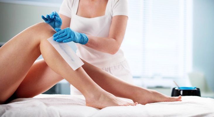 Person in gloves waxing a leg with wax strip.