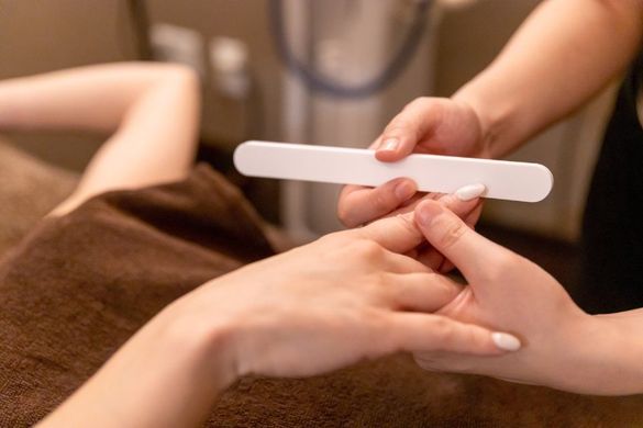 Hands receiving manicure: Nail file being used on a person's fingernail.