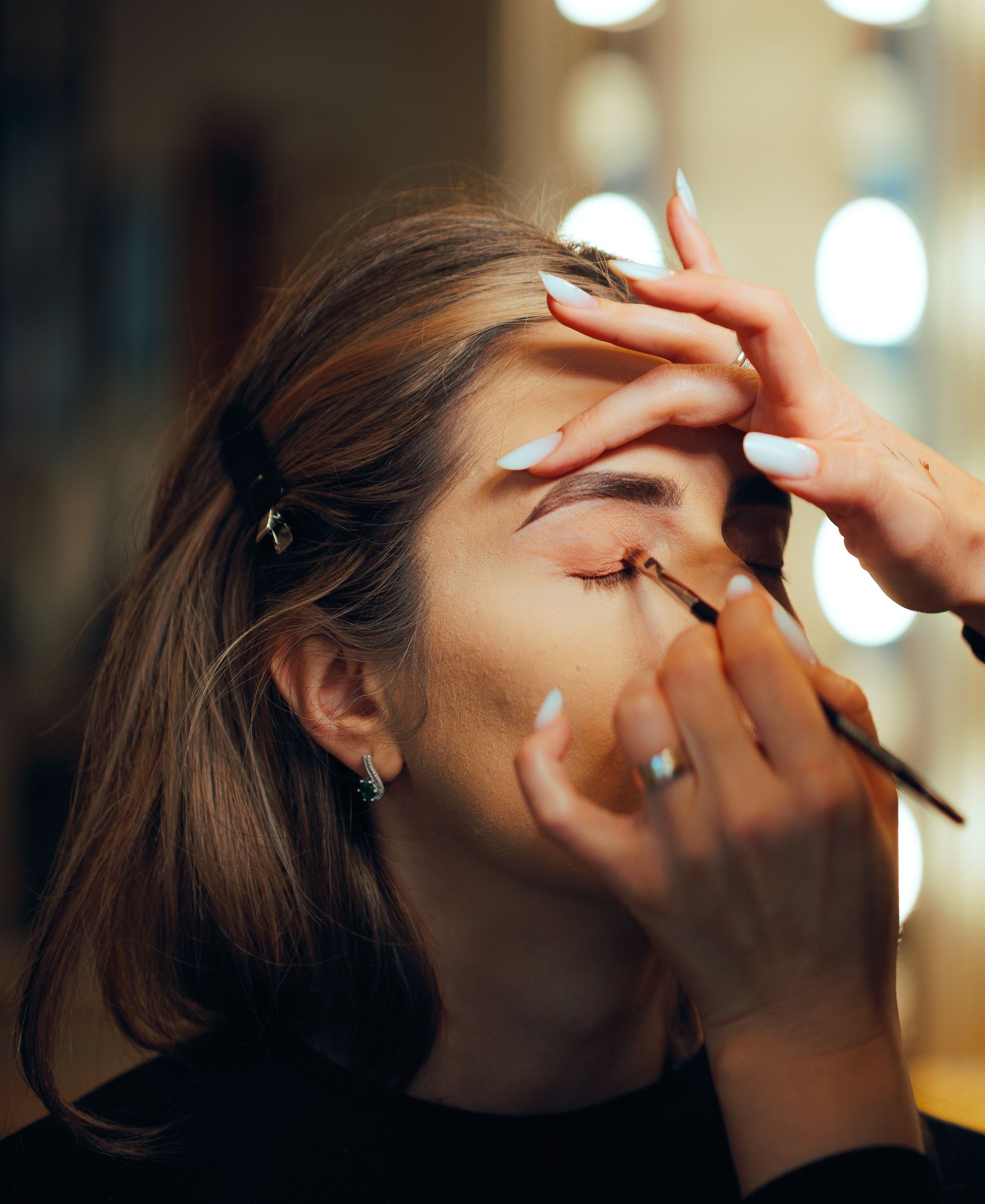 Makeup artist applying eyeshadow to a person's closed eye with a brush.