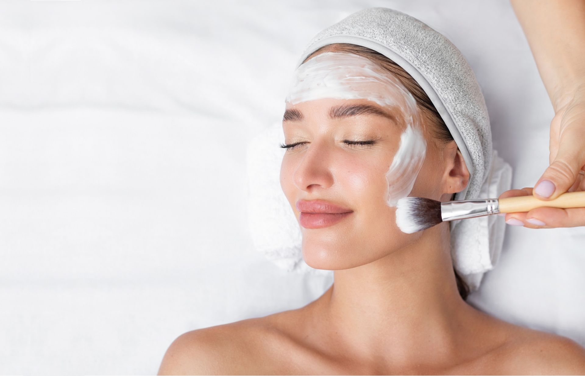 Woman receiving facial treatment, cream being applied with a brush.