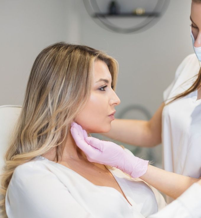 Woman receiving a facial examination by a gloved person; light pink gloves, white tops.