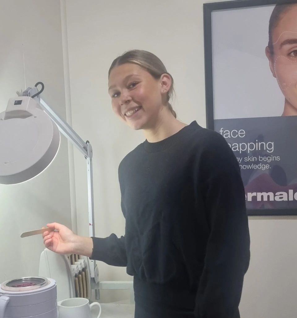 Woman holding a wax spatula in a beauty treatment room, smiling.