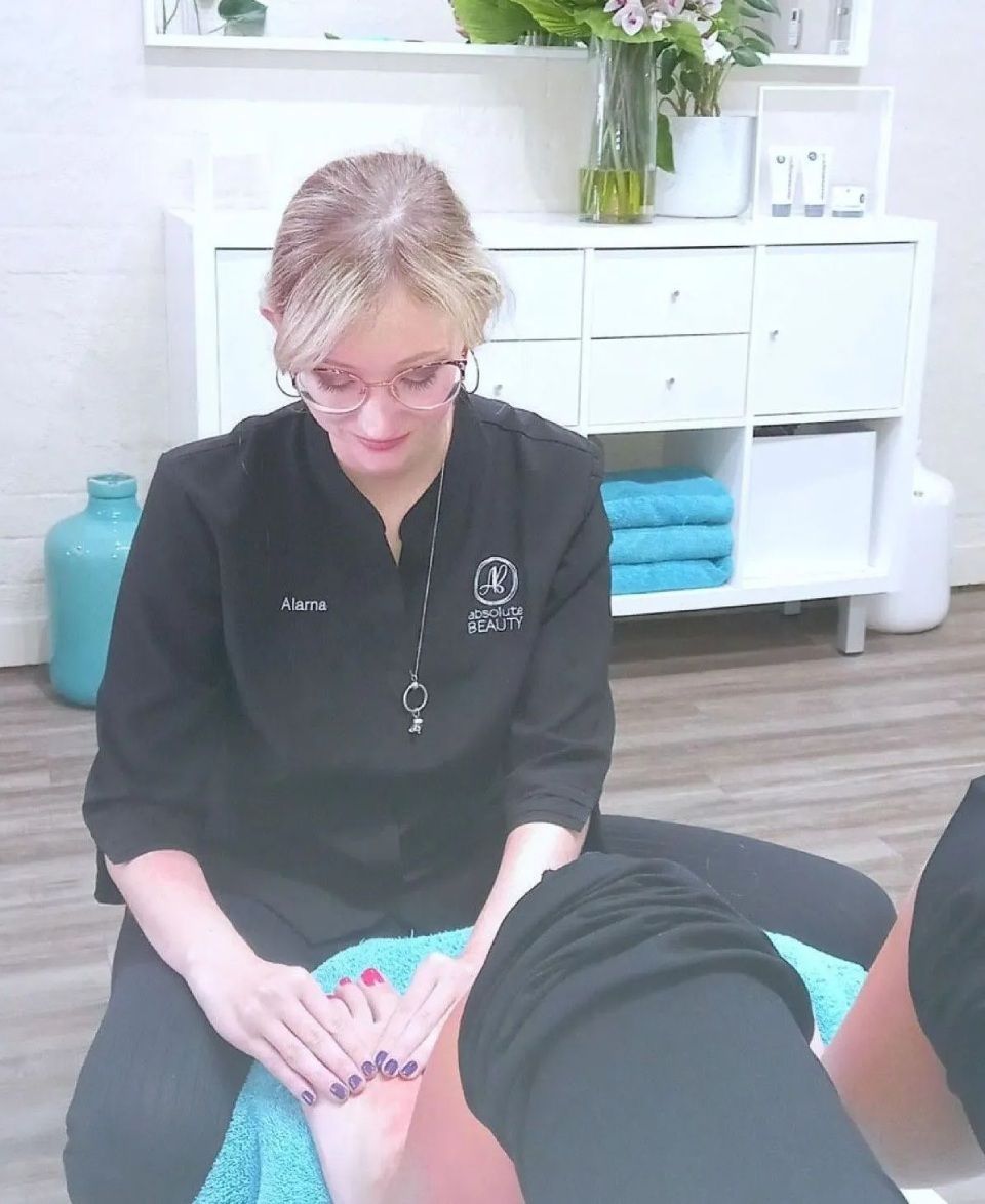 Woman giving foot massage in spa. Dark uniform, glasses. Hands on feet with painted nails. Bright room.