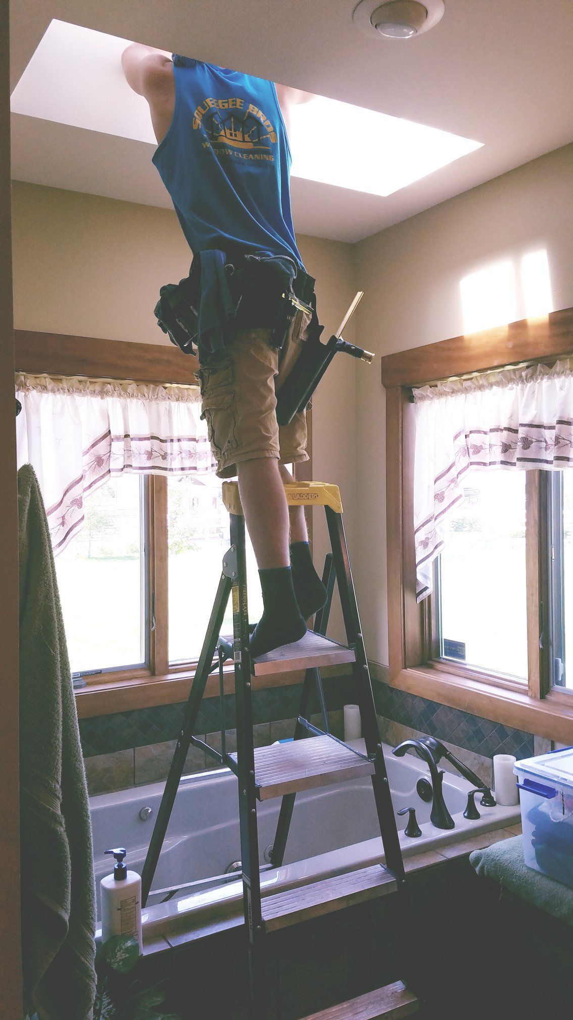 A man standing on a ladder in a bathroom with a batman shirt on