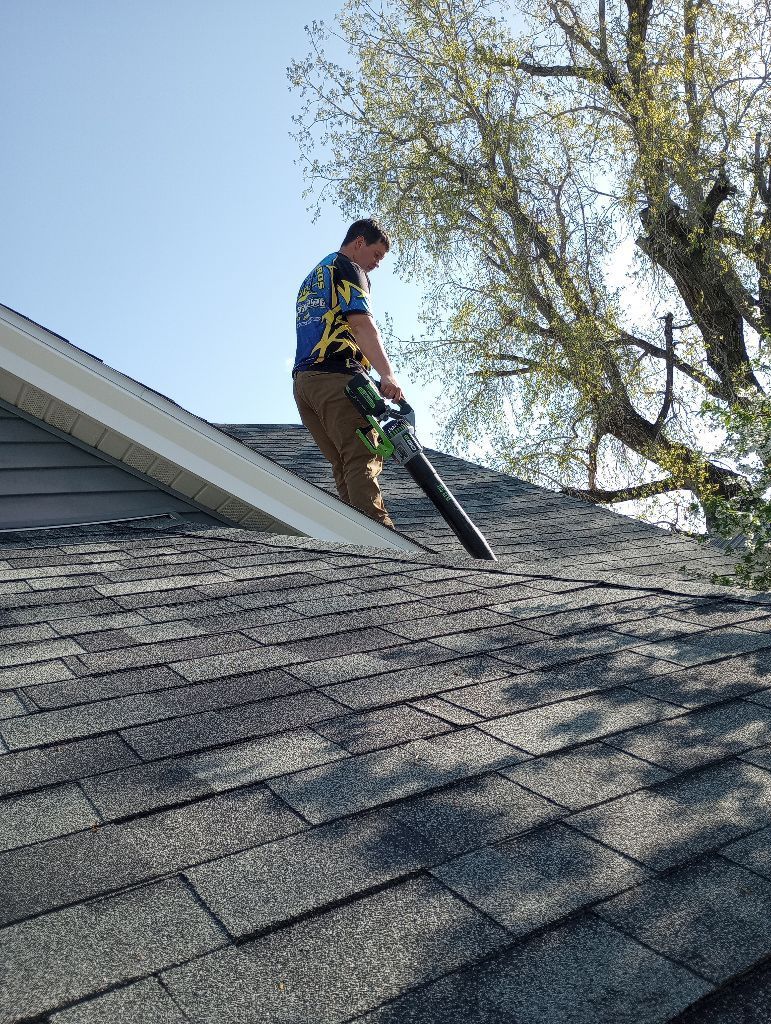 A man is standing on a roof using a blower