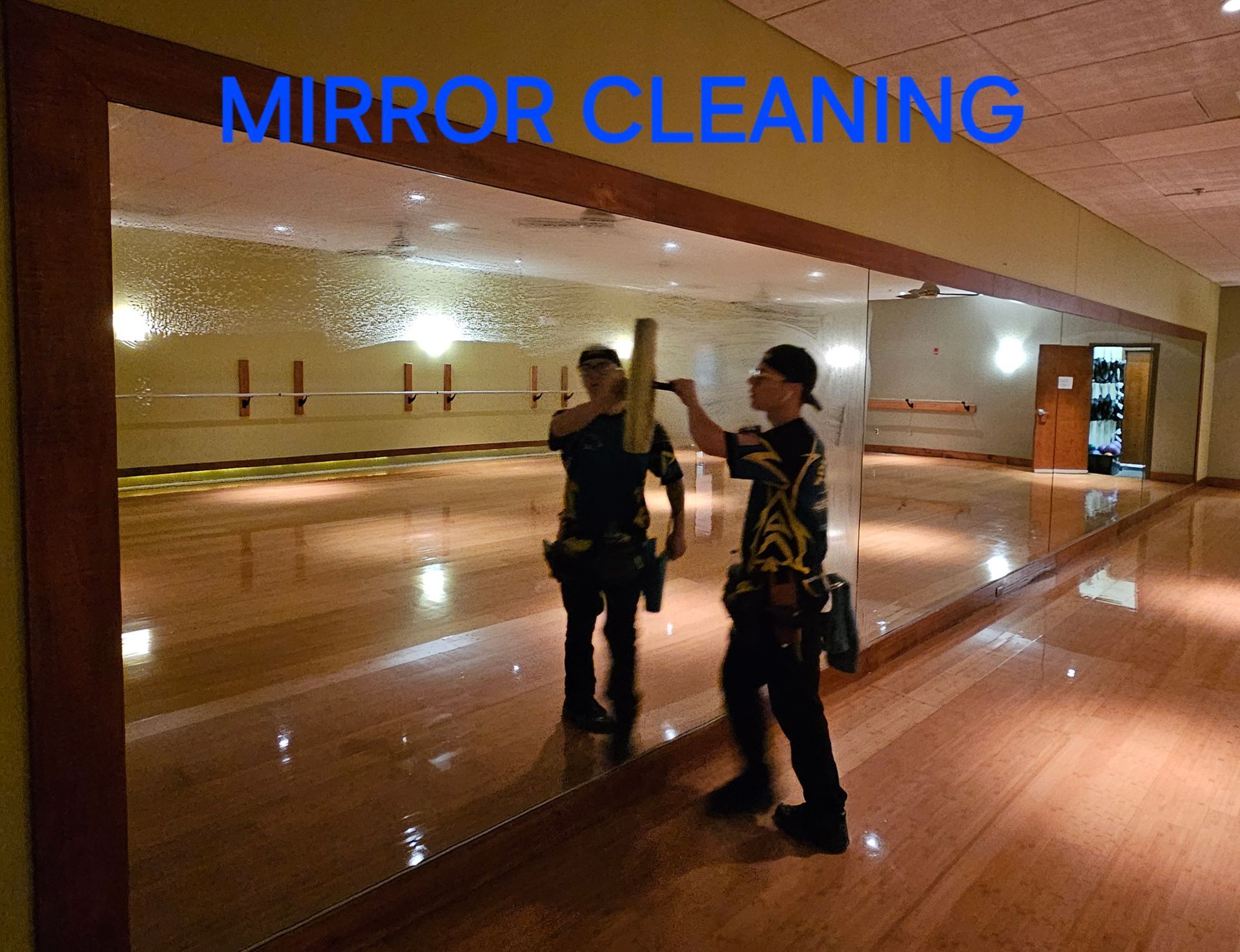 A man is cleaning a large mirror in a gym