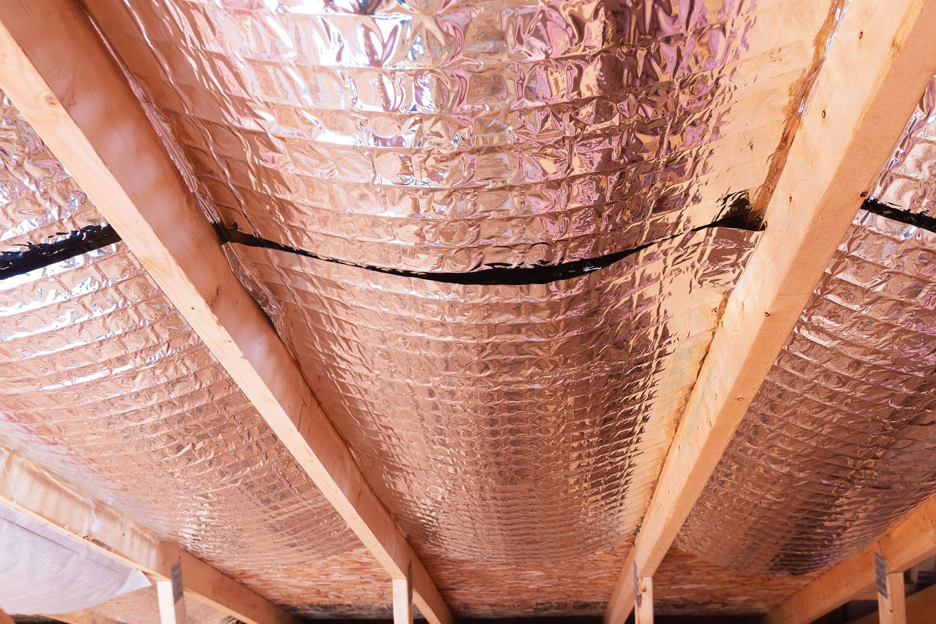 Foil-faced insulation installed between wooden roof rafters in an attic space