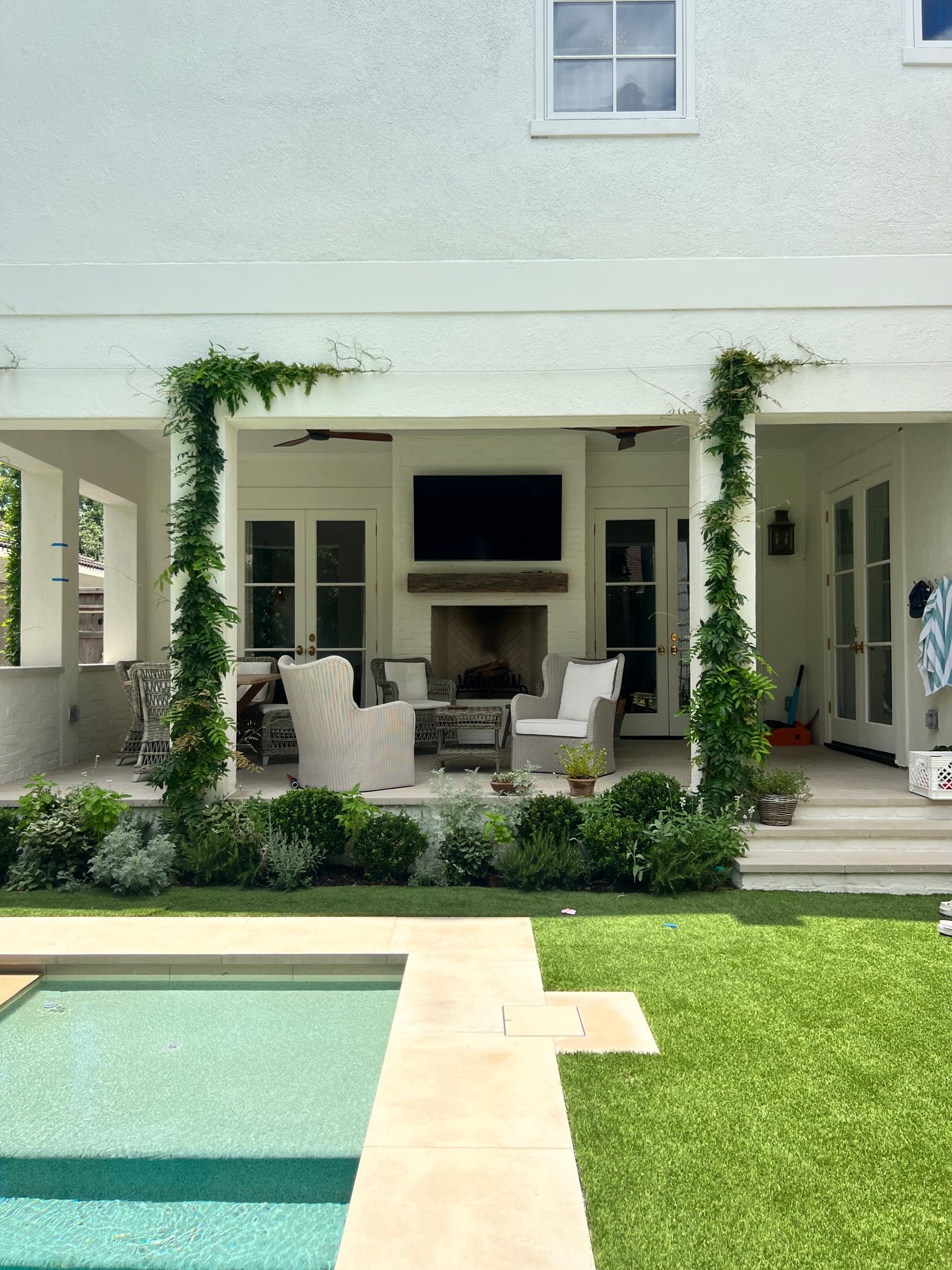 Backyard patio with outdoor seating, fireplace, pool, and green lawn under a covered veranda