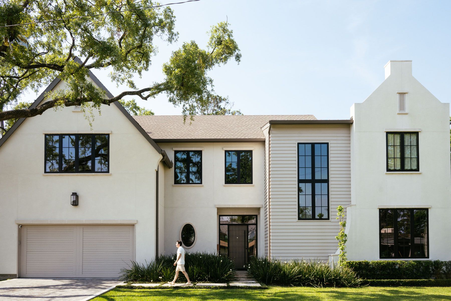Modern white two-story house with garage, large windows, and a person walking on the front lawn