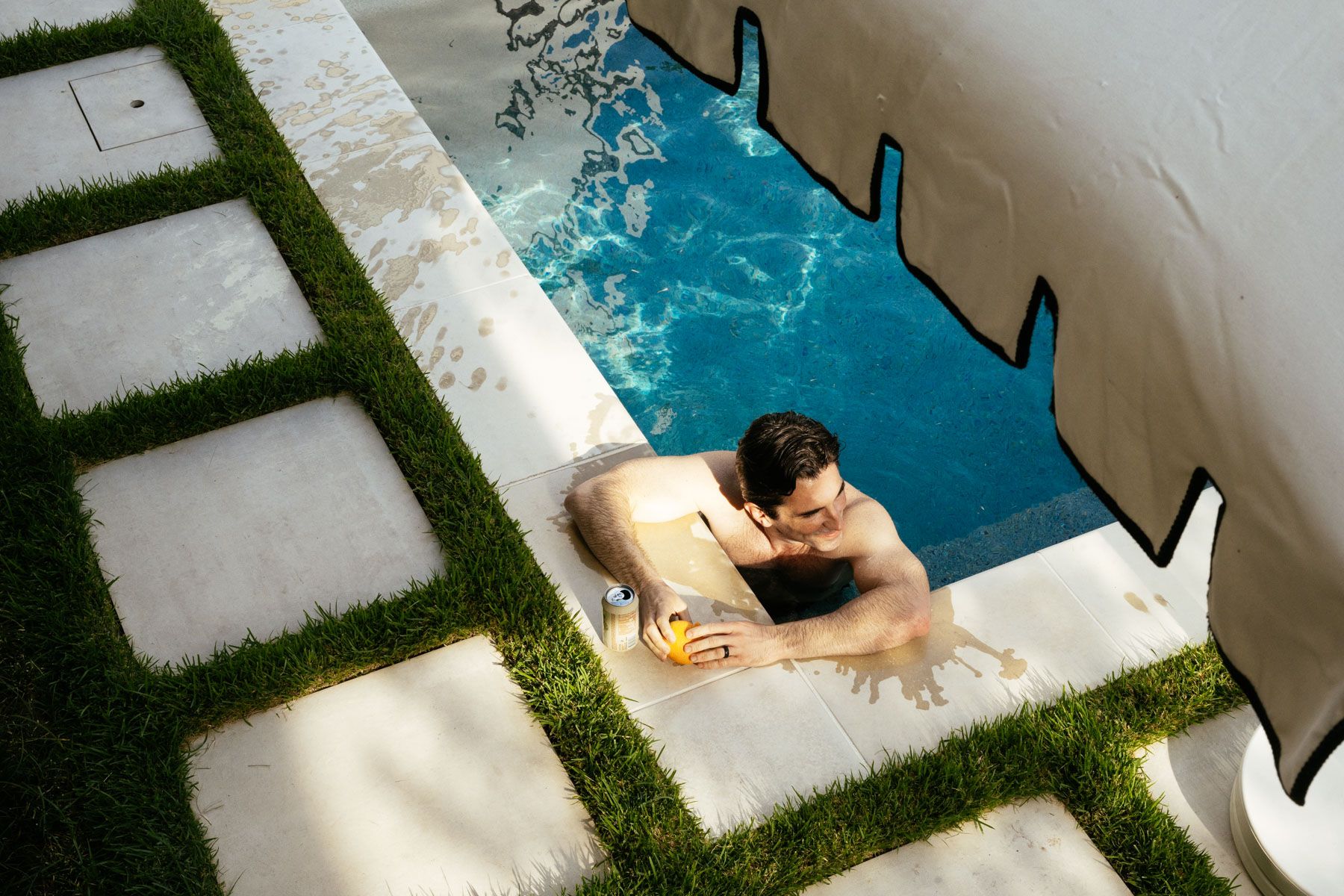Person in a pool climbing the steps beside green-tiled walkway and white wall.