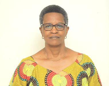 A woman wearing glasses and a yellow shirt is standing in front of a white wall.