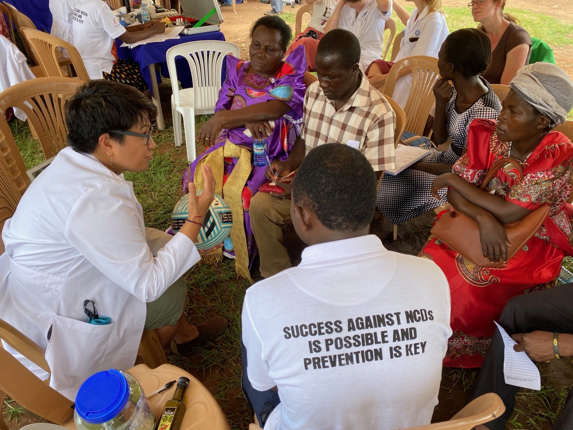 A group of people are sitting around a table with a man wearing a shirt that says success against malaria