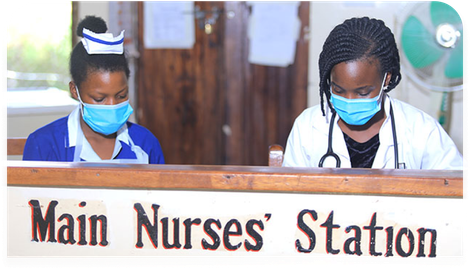 Two nurses wearing masks are sitting at the main nurses station
