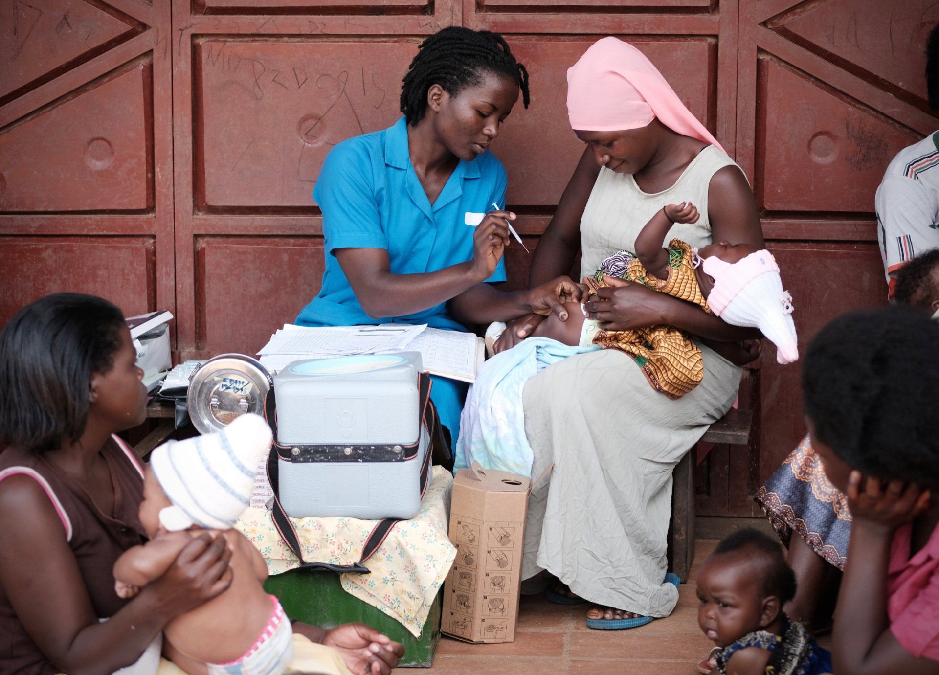 A woman is holding a baby while a nurse gives it an injection