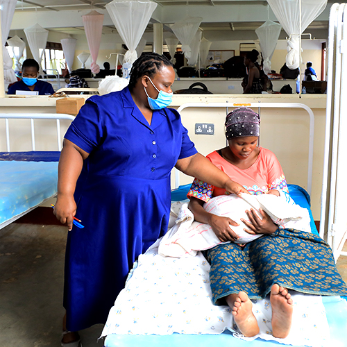 A woman wearing a mask is holding a baby in a hospital bed.
