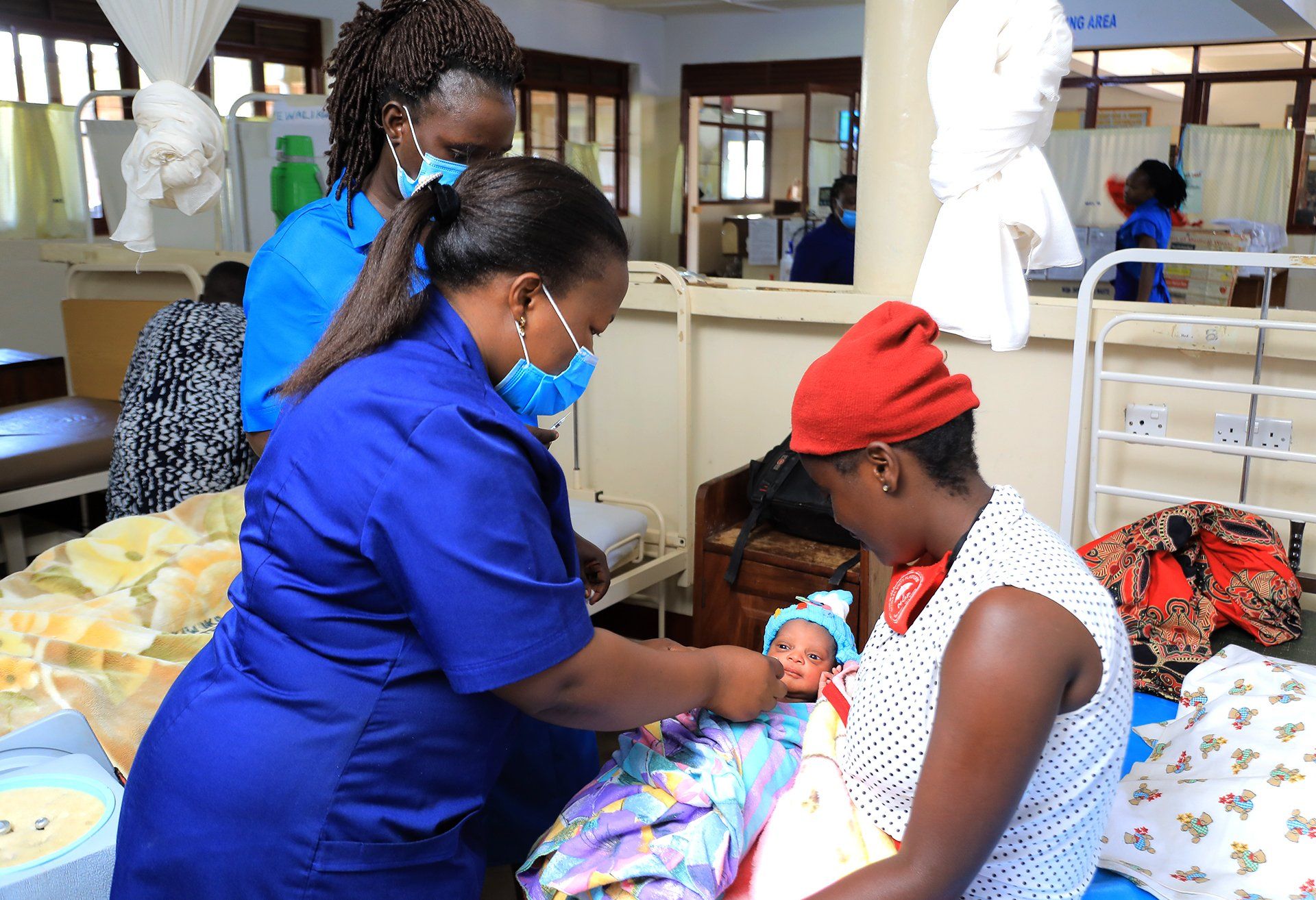 A woman is holding a baby in a hospital room while a nurse examines it.