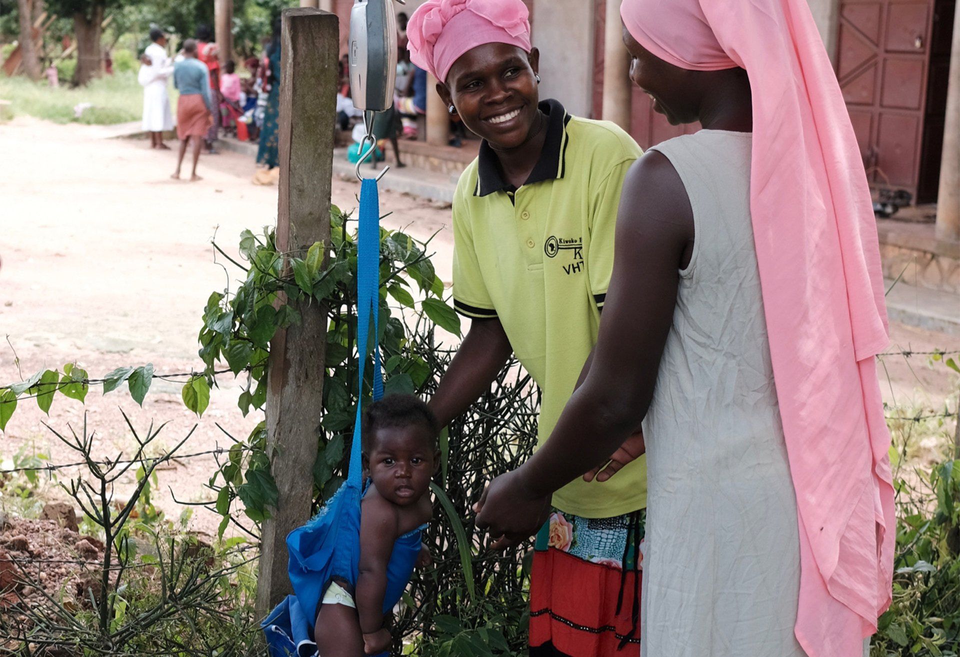 A woman in a pink head scarf is holding a baby