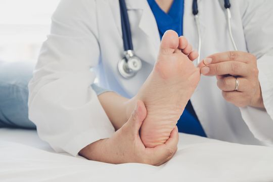 A doctor wearing a mask is examining a patient 's foot.
