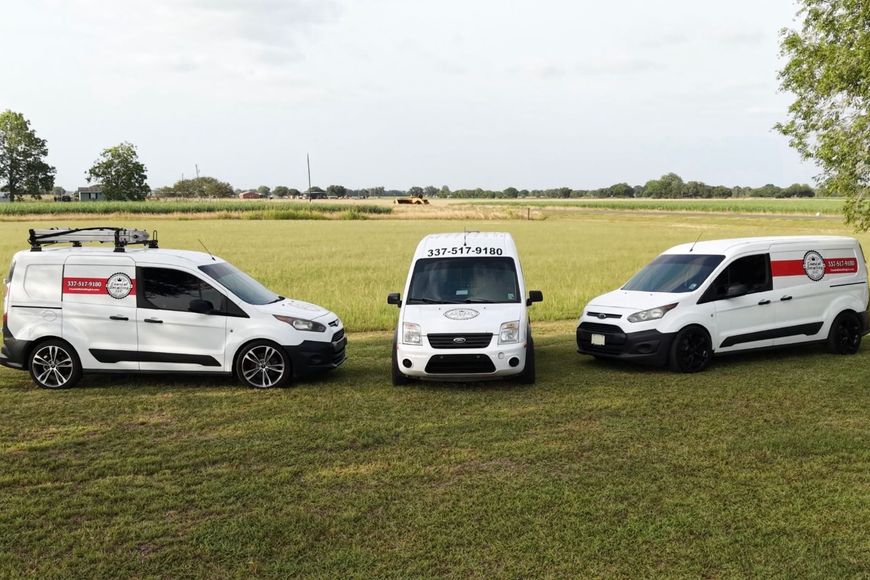 Three white utility vans parked on a grassy field under an overcast sky