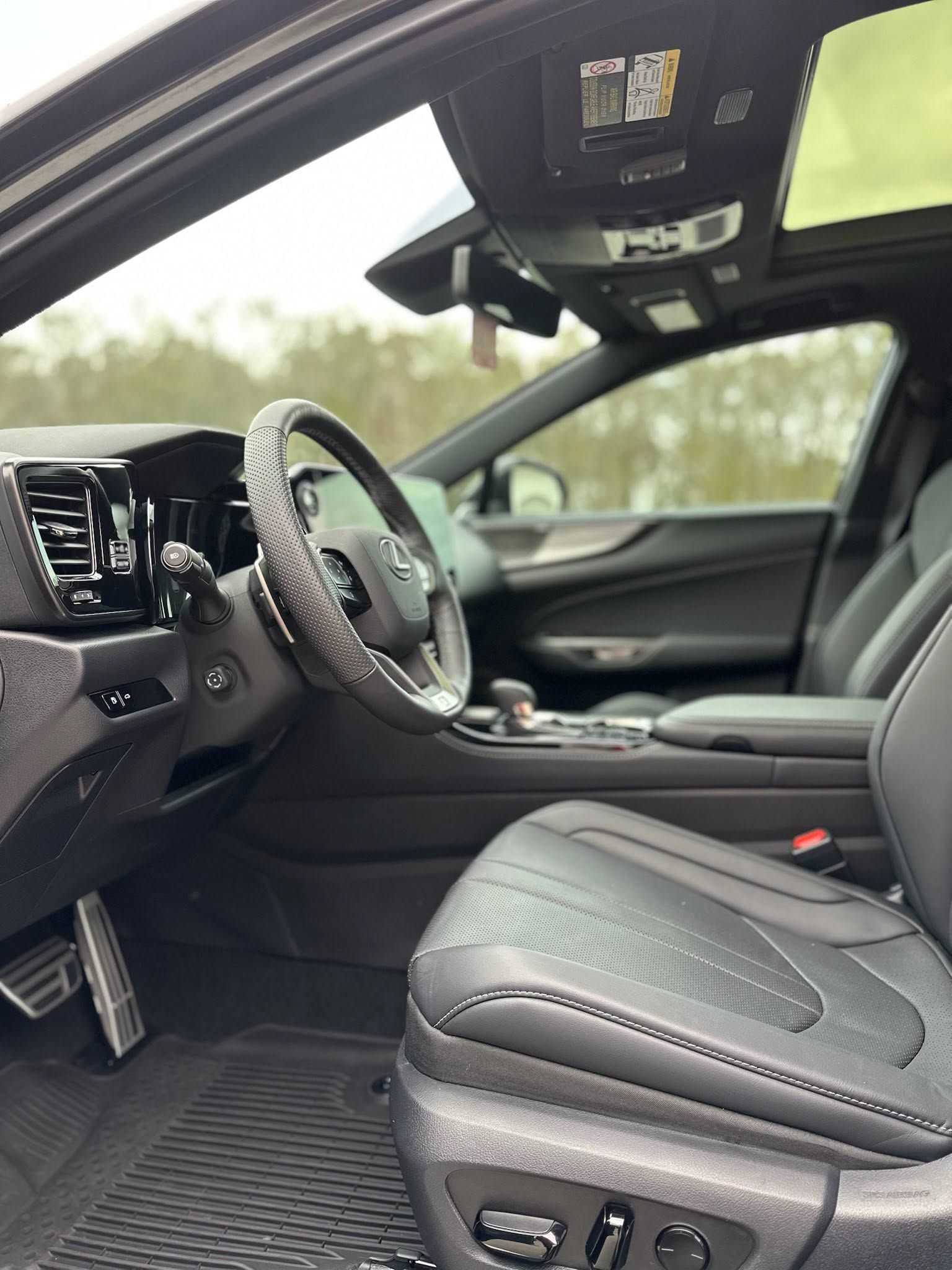 Luxury car interior with black leather seats, steering wheel, and dashboard viewed from the open driver’s door