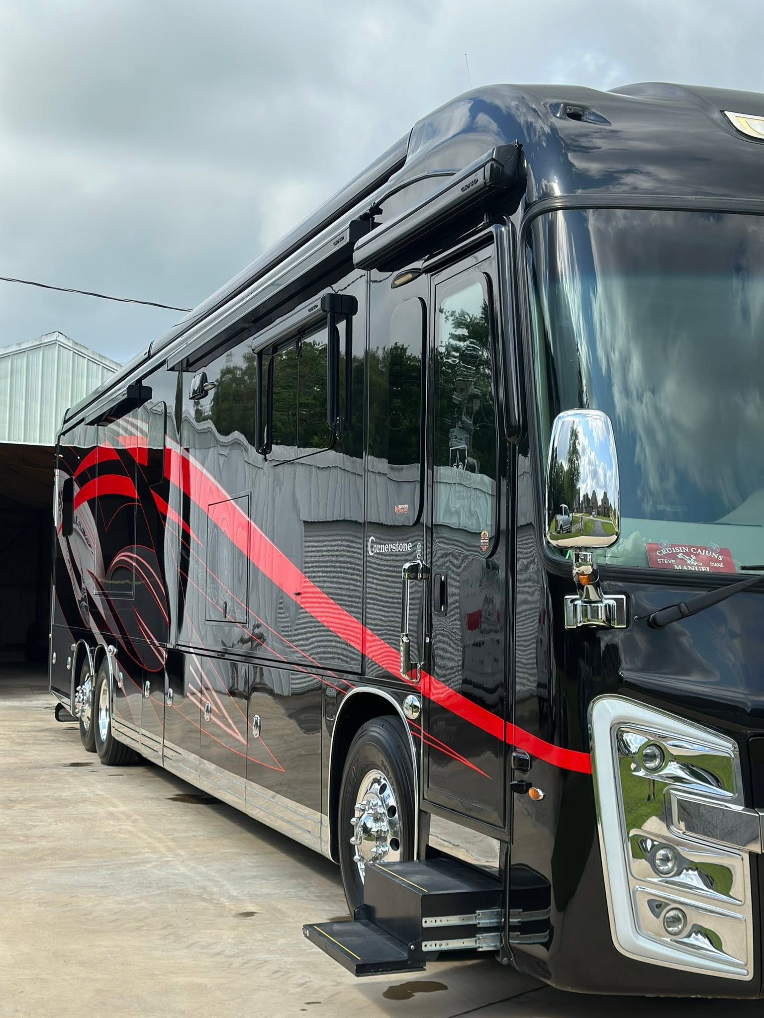 Black luxury tour bus with red stripe parked outdoors under cloudy sky