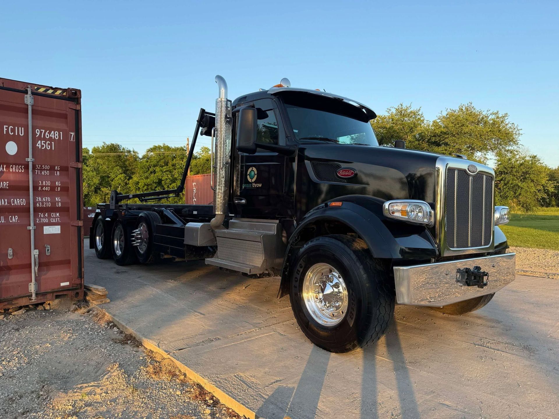 Black semi-truck parked beside shipping containers in a lot, viewed from the front-left.