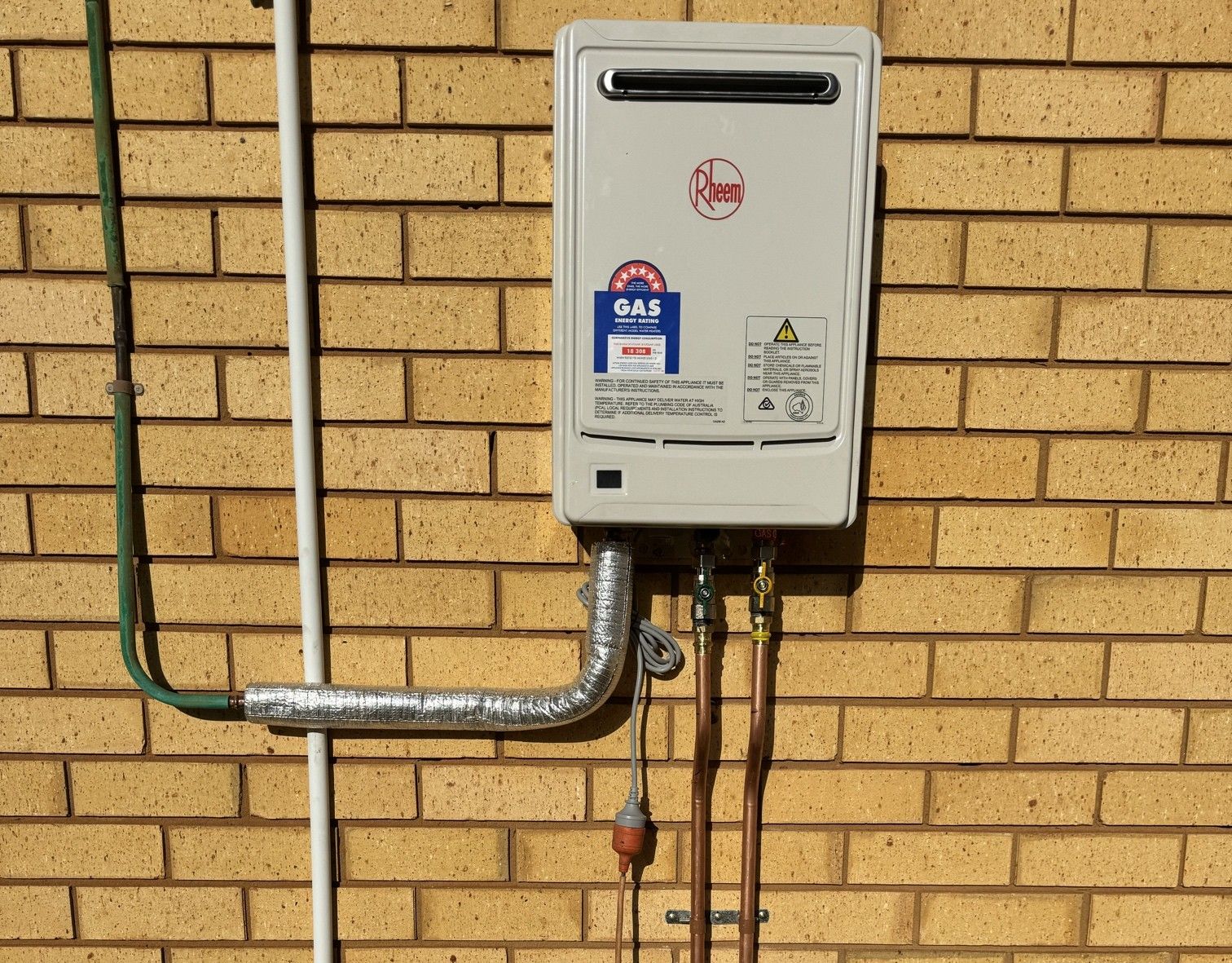 Wall-mounted gas meter box and pipes on a yellow brick exterior wall.