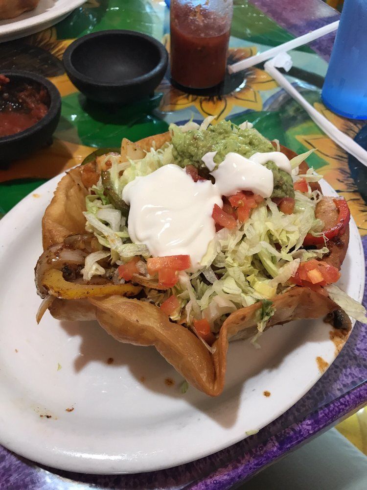 Taco salad in a fried tortilla bowl on a white plate, topped with lettuce, sour cream, and guacamole.