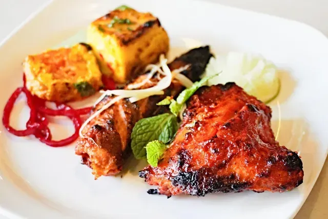 Grilled Indian-style meat and paneer dish on a white plate, with red onions and lime.