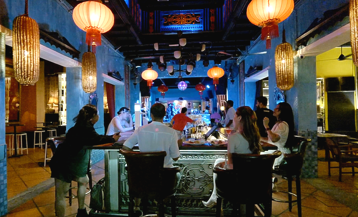 People dining at a Chulia Court bar under red lanterns in a dim, blue-lit restaurant