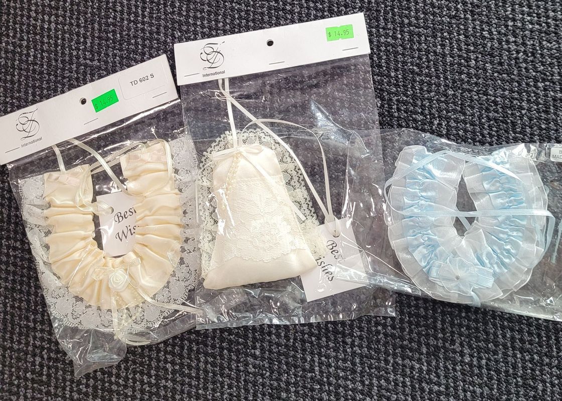 Three wrapped items: ivory ribbon scrunchie, white pouch with beads, and blue coiled item. All have tags. - Shona's Lingerie, Townsville, QLD.
