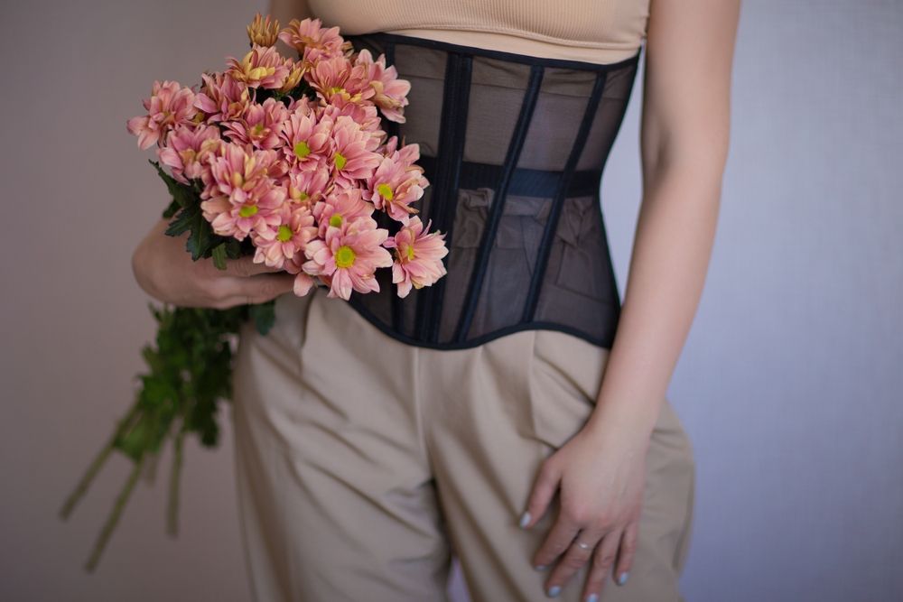 Woman in Corset and Beige Pants, Holding Pink Flowers — Shona's Lingerie in Hermit Park, QLD