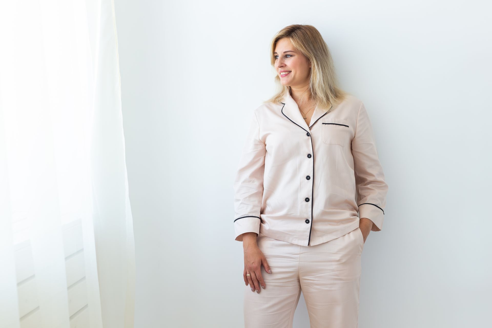 Woman in pink pajamas leans against a white wall, smiling — Shona's Lingerie in Hermit Park, QLD