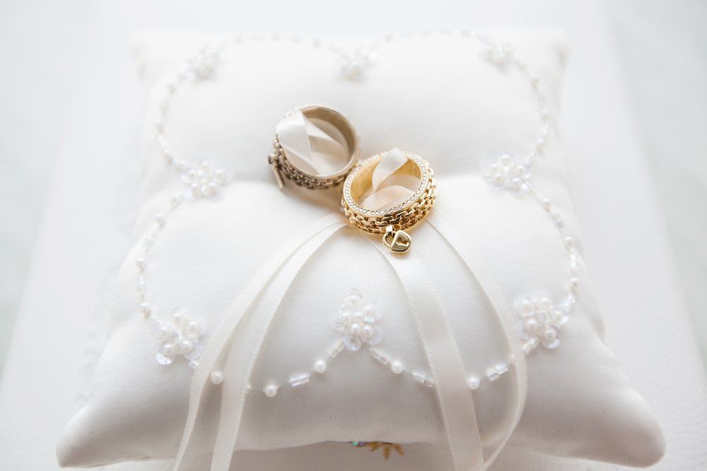 Two Gold Wedding Rings on a White, Embroidered Ring Pillow With Ribbons — Shona's Lingerie in Hermit Park, QLD