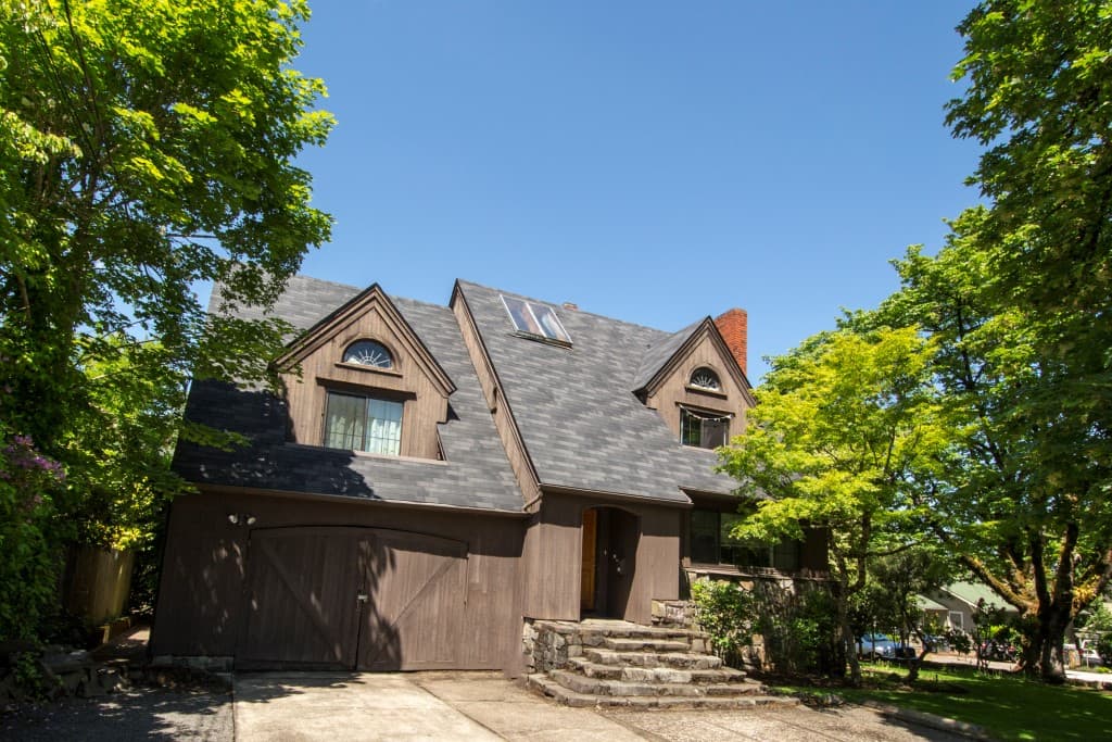 A brown, 2 story traditional style home with brown garage door, pointed roofline, and blue sky