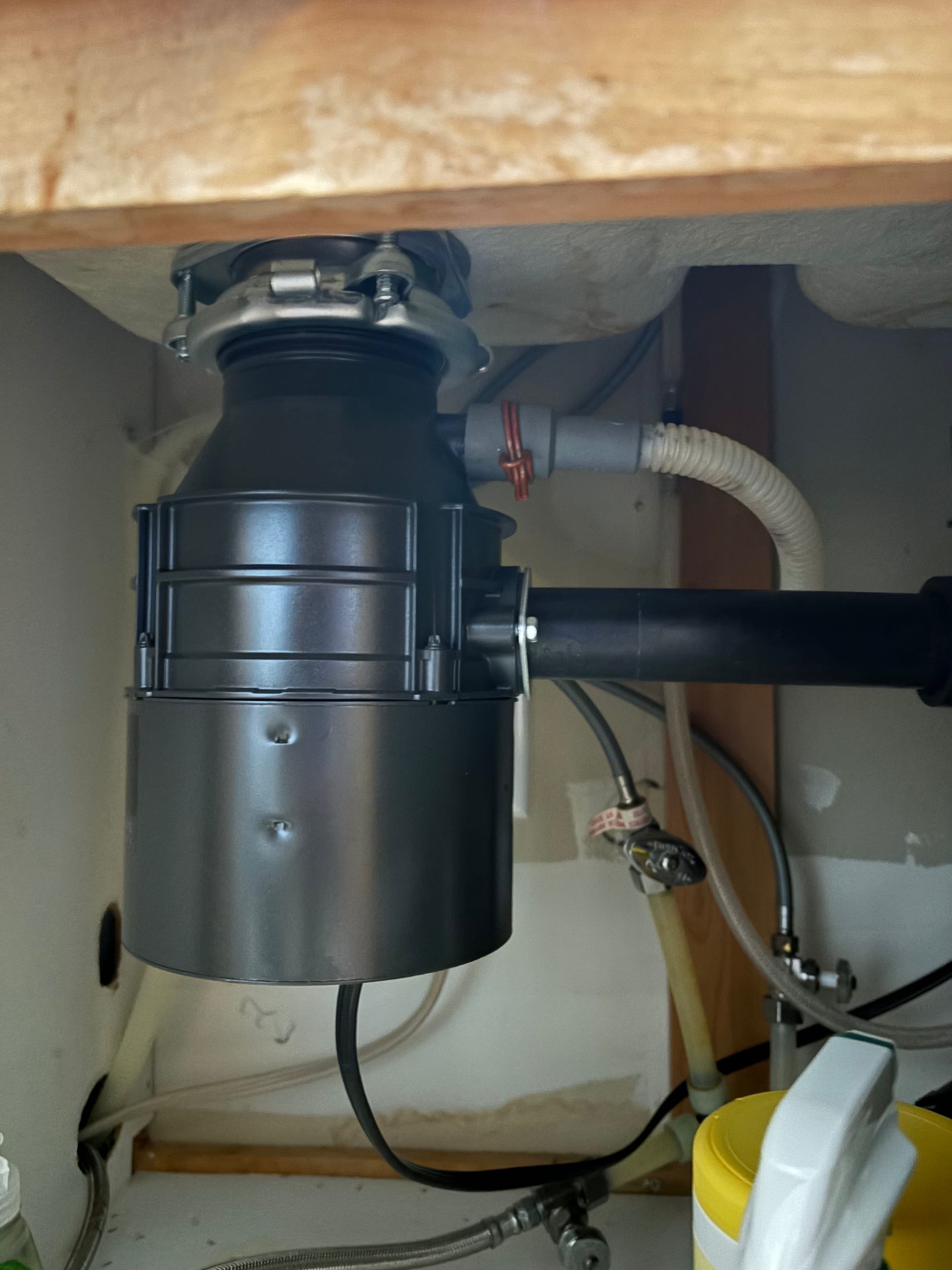 A garbage disposal below a sink cabinet with plumbing visible