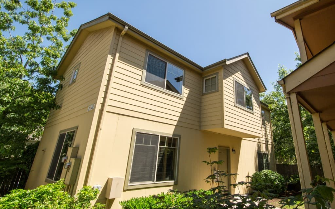 A two story rental unit with yellow lap siding, green trees, and blue sky