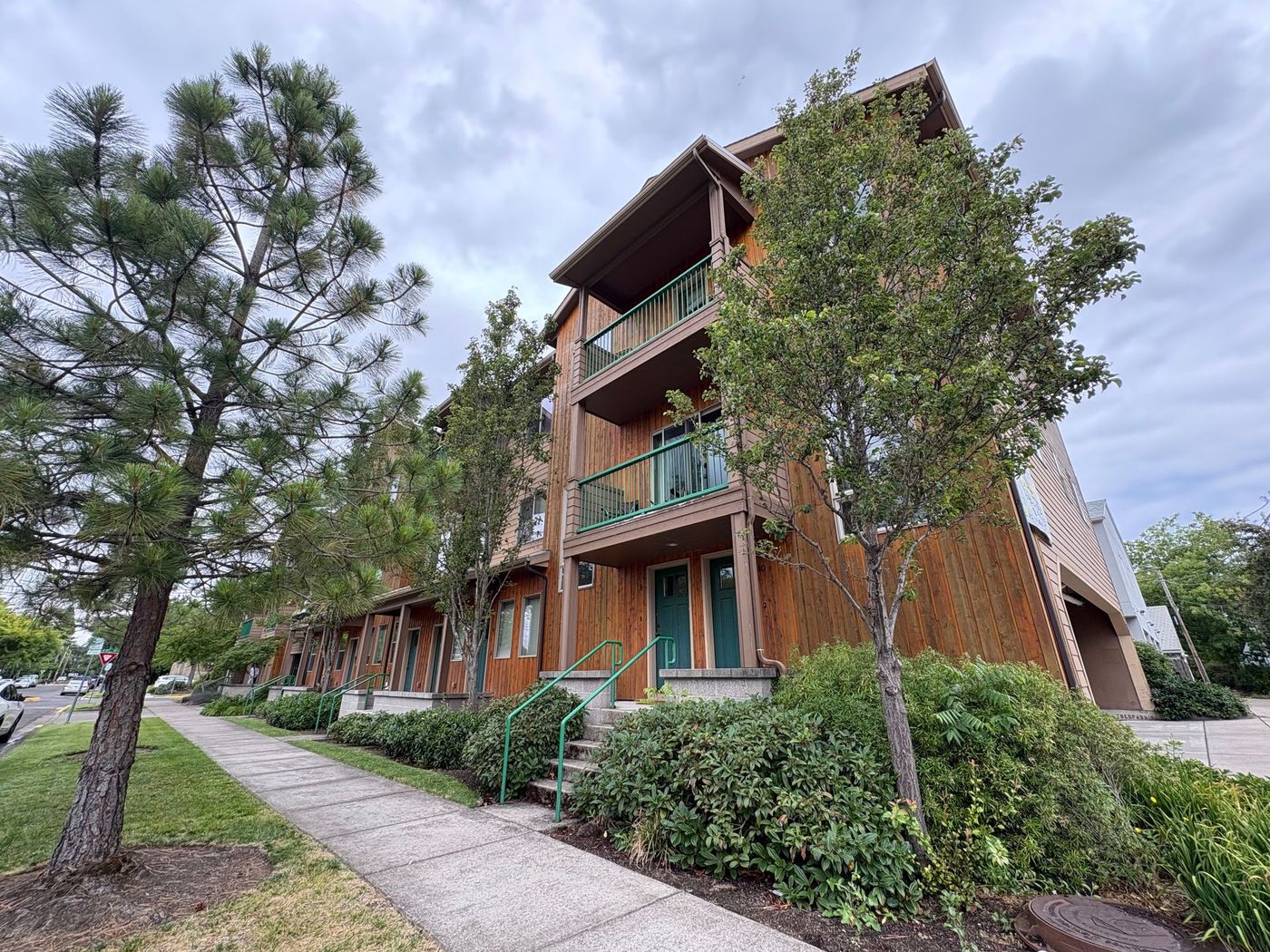 An apartment complex with brown vertical siding, dark green front doors, and green pine trees
