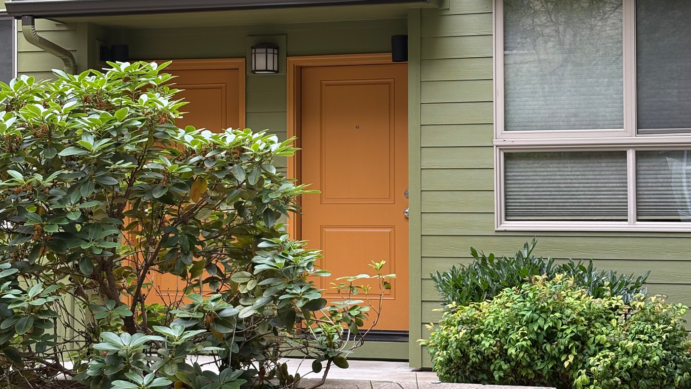 Two yellow front doors in an apartment complex with green siding and bushes