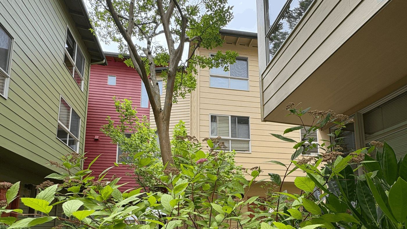 An apartment complex exterior with beige and red siding, with green trees and bushes