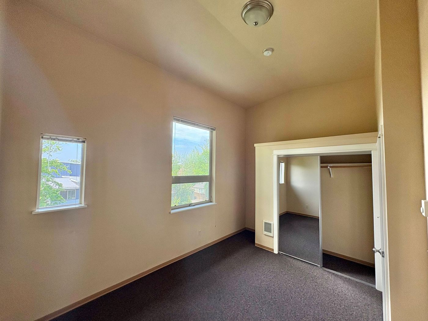 A bedroom with two windows, a closet, and tall ceilings