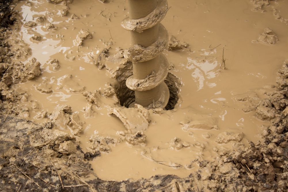 Auger drill boring into saturated muddy ground on a construction site.