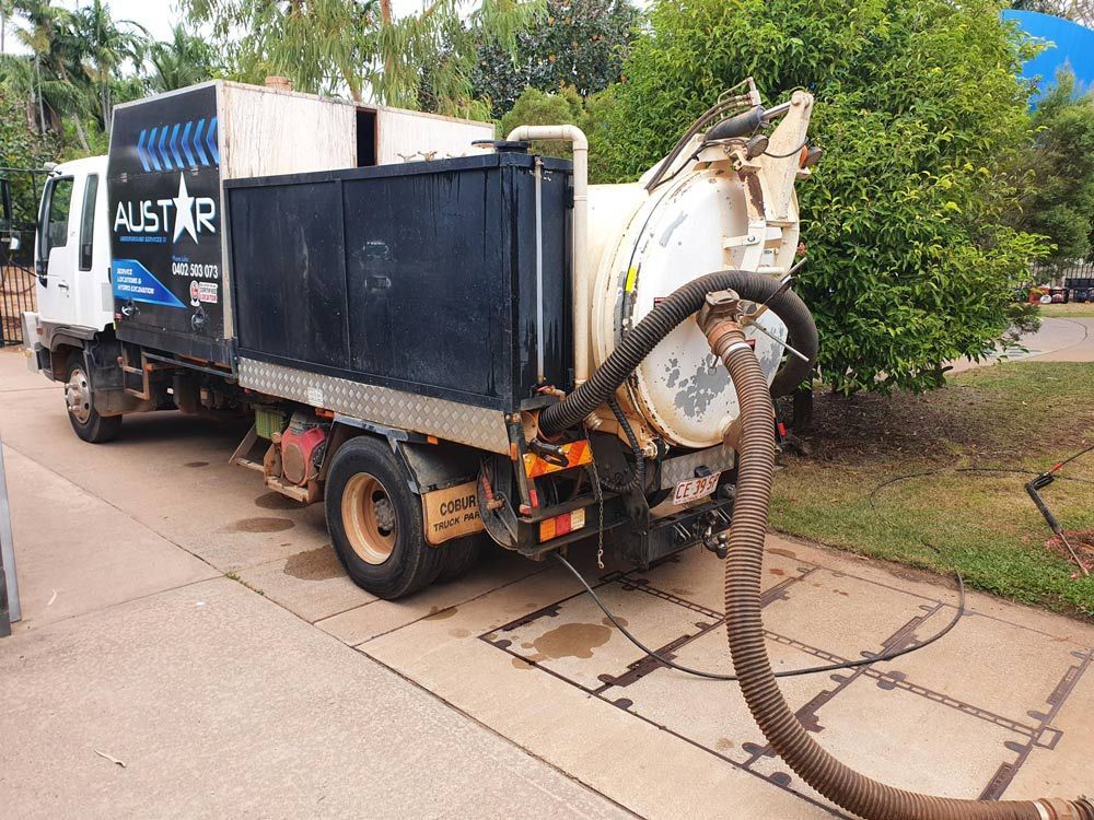 A vacuum truck parked on a paved area with its hose extended. It has the name 