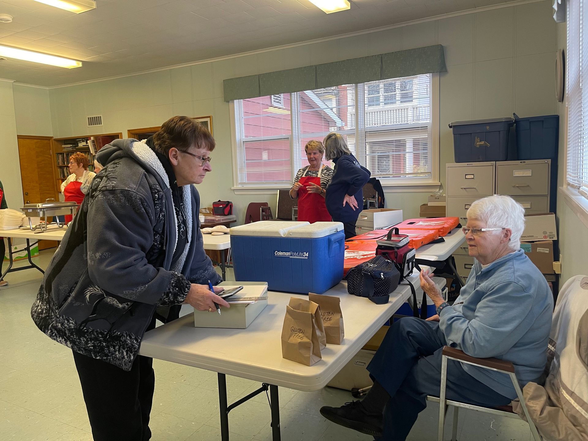 People at a table in a room, with a blue bin and boxes during a community activity.