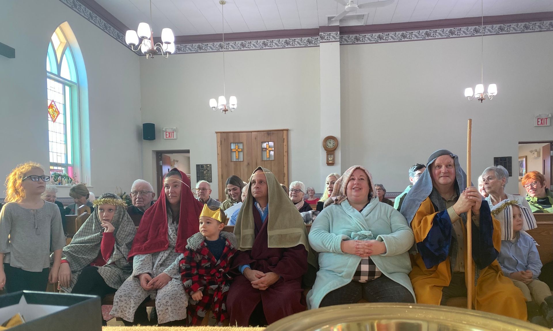 People seated in a church hall, many smiling and wearing colorful hats and costumes