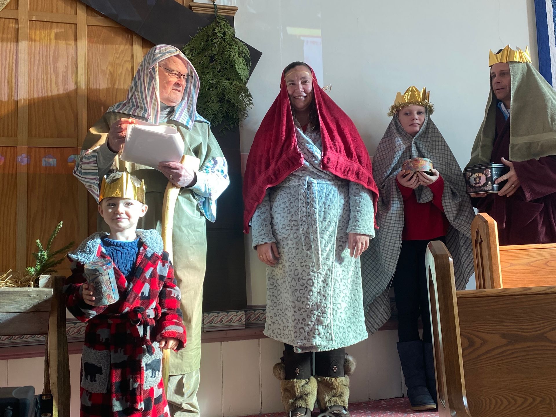 Five people in costumes stand on a small stage, wearing crowns, robes, and holding props.