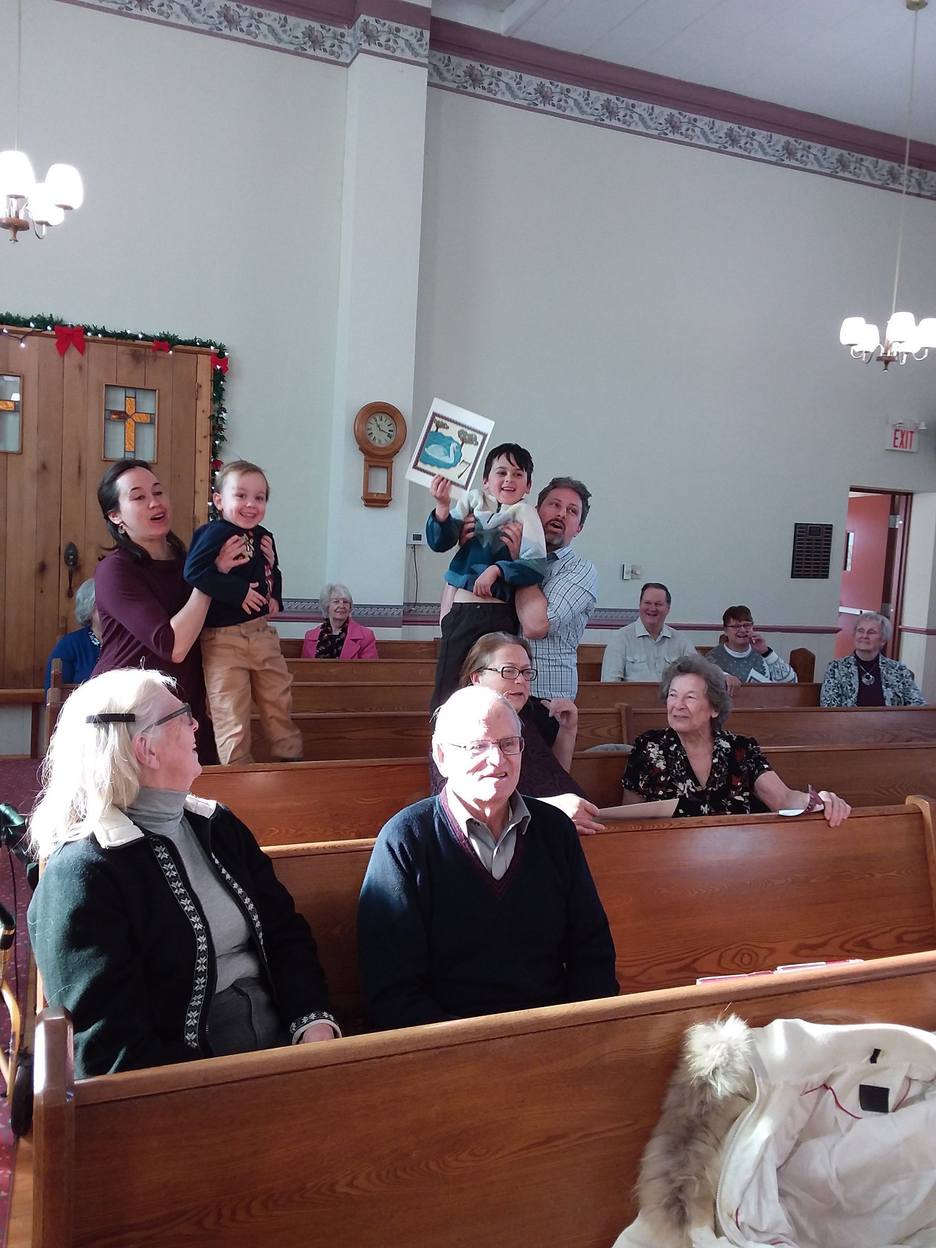 People seated in wooden pews inside a church, with a few standing near the back.